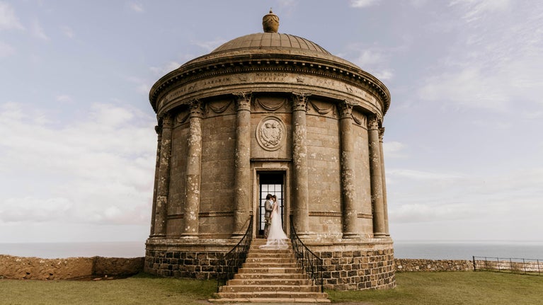 An image of a bride and groom standing at the steps of Mussenden Temple.